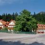 A large house with red roofs and balconies, surrounded by trees and a forest in the background.