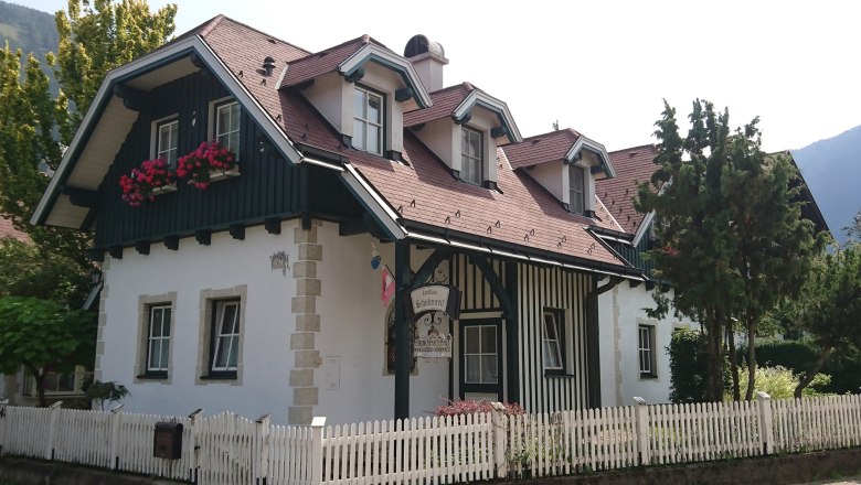 Country house Scheibenreif, © Scheibenreif Karin A traditional country house with wooden cladding, red roof tiles and flower boxes in front of the windows. A white wooden fence surrounds the property.