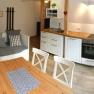 Cozy kitchen with wooden table, white chairs, sofa and modern kitchenette.