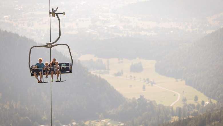 Eltern sitzen mit ihrem kleinen Sohn und ihrer kleinen Tochter in der Schneeberg Sesselbahn