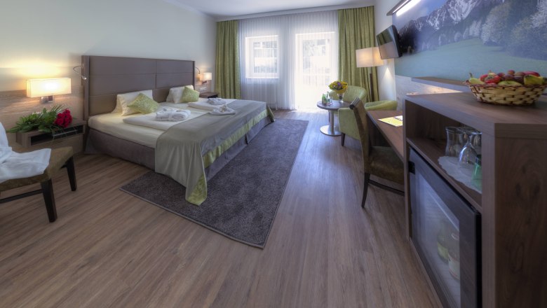 Elegantes Hotelzimmer mit Doppelbett, Sitzbereich und gro&szlig;em Fenster.