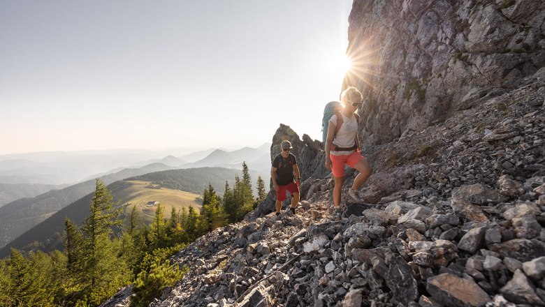 Mann und Frau wandern auf dem Schneeberg. Im Hintergrund die Morgensonne