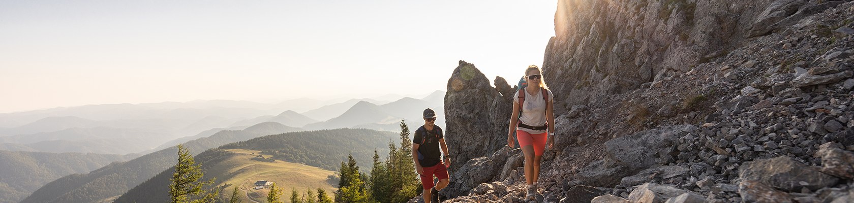 Mann und Frau wandern im Gipfelbereich mit Sonne im Hintergrund