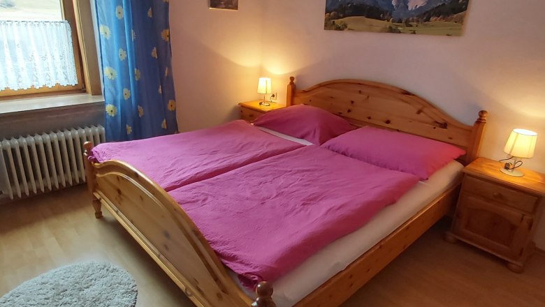 Gem&uuml;tliches Doppelzimmer mit Holzbett, pinker Bettw&auml;sche und Nachttischen mit Lampen.