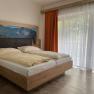 Modern double room with large bed, mountain picture on the wall and large windows with curtains.