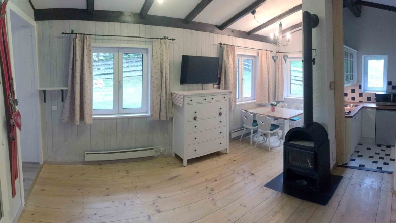 Innenansicht eines gem&uuml;tlichen Ferienhauses mit Holzofen, Esstisch und K&uuml;che.