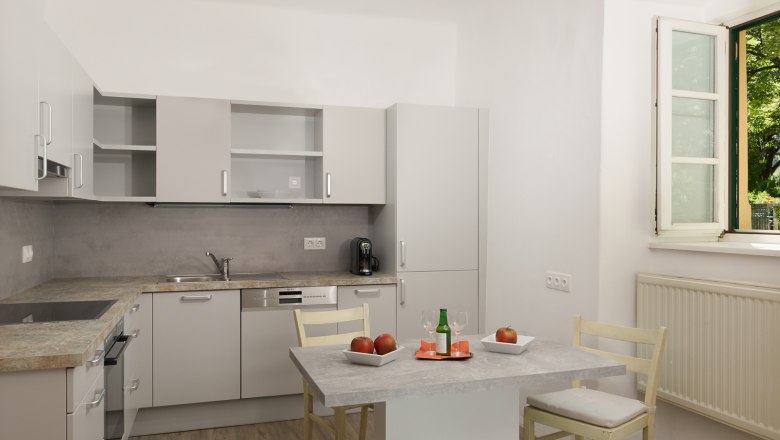 Moderne K&uuml;che mit grauen Schr&auml;nken, Tisch mit &Auml;pfeln und Getr&auml;nk, offenes Fenster.