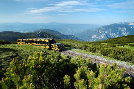 Der Salamander-Zug der Schneebergbahn mit Bergpanorama im Hintergrund.