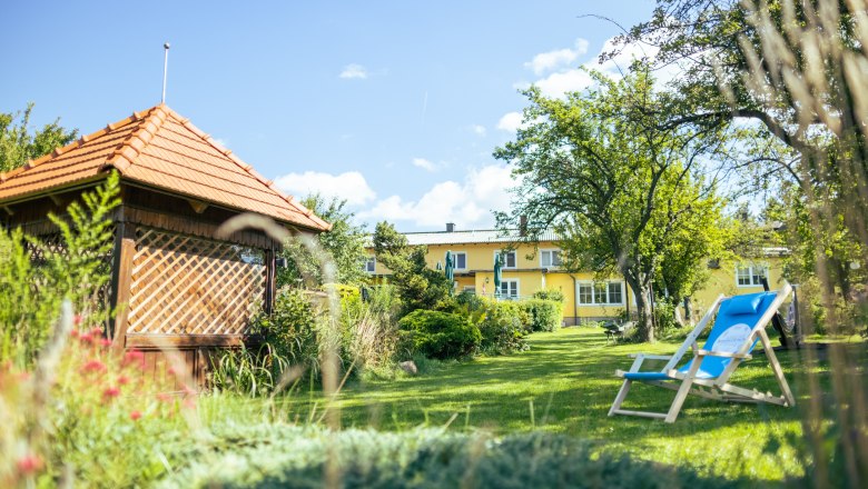 Garden of the senses - Gasthof Schmirl, © Martin Fülöp A green garden with a pavilion, deckchairs and a yellow building in the background.