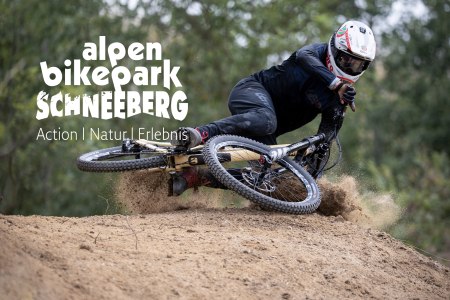 Mountainbiker in schwarzer Schutzkleidung und Helm fährt in Kurve auf Dirt-Trail im Alpen Bikepark Schneeberg.
