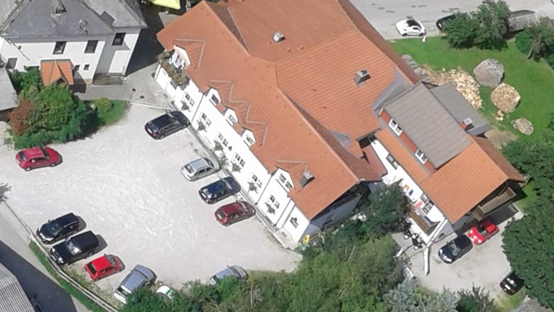 Luftaufnahme eines Geb&auml;udekomplexes mit roten D&auml;chern und mehreren geparkten Autos auf einem Parkplatz.