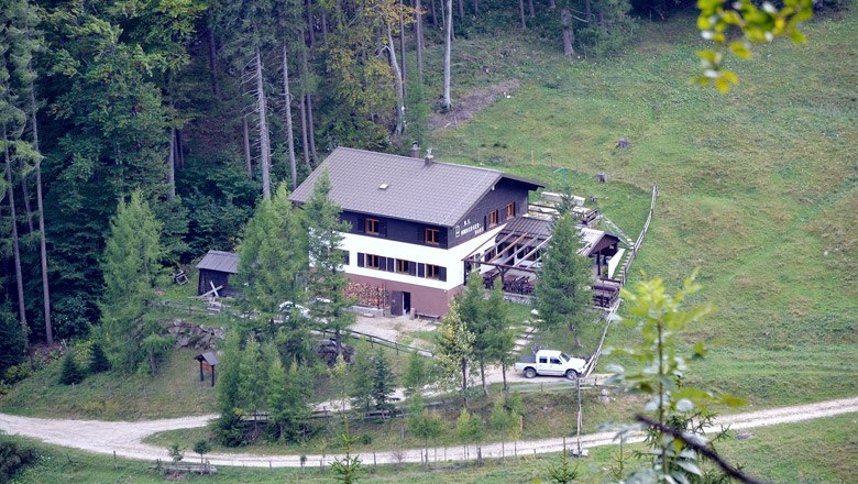 Ein gro&szlig;es Haus im Wald mit einem Auto davor, umgeben von B&auml;umen und Wiesen.