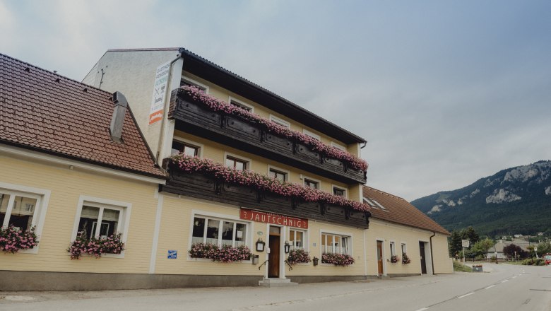 Country inn at the foot of the Hohe Wand, © Niederösterreich Werbung/Rita Newman A traditional country inn with balconies decorated with flowers against a mountain backdrop.