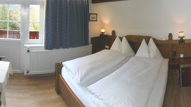 Gem&uuml;tliches Schlafzimmer mit Doppelbett, Holzm&ouml;beln und Fenster mit Blick ins Gr&uuml;ne.