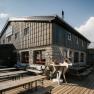 A fisherman's cabin on Schneeberg with a terrace, benches, and a decorative ibex statue in front of the building