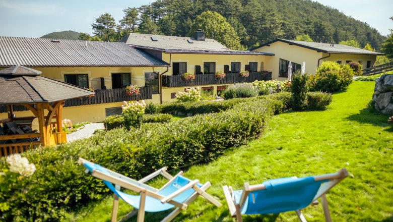 Zwei blaue Liegest&uuml;hle auf einer gr&uuml;nen Wiese vor einem gelben Geb&auml;ude mit Blumen auf den Balkonen.