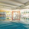 Ein helles Hallenbad mit Liegestühlen und einem Wasserstrahl im Pool.