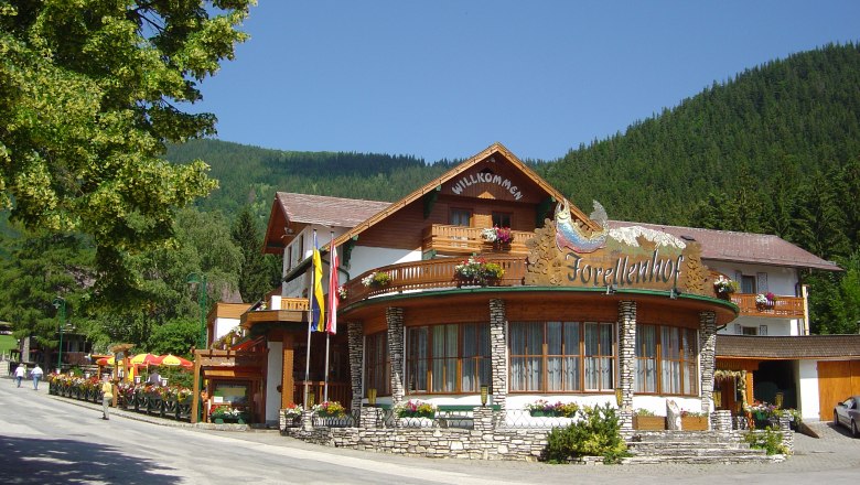 Hiking hotel Forellenhof, © Forellenhof A traditional hotel with a wooden façade and flowers, surrounded by mountains and trees.