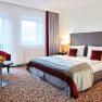Doppelzimmer im Hotel Schneeberghof mit Doppelbett, roten Kissen, Tisch mit Obstschale und zwei Sesseln.